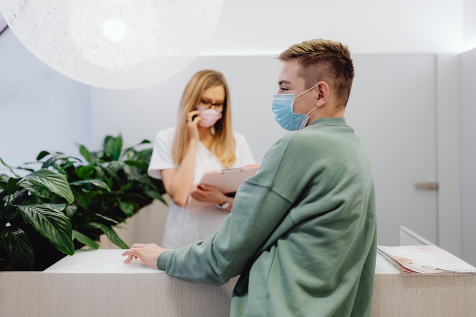 A patient and receptionist in a clinic wearing face masks, ensuring health safety.
