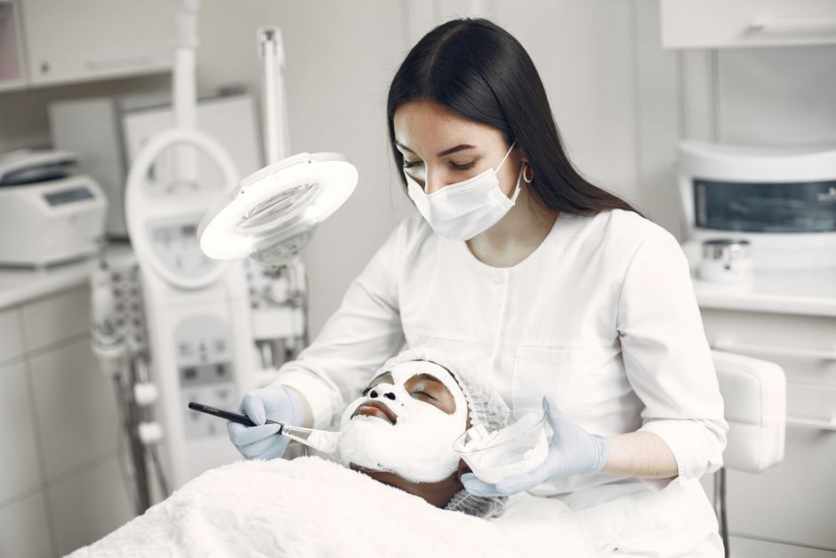 A spa professional applying a facial mask to a client in a modern clinic setting.